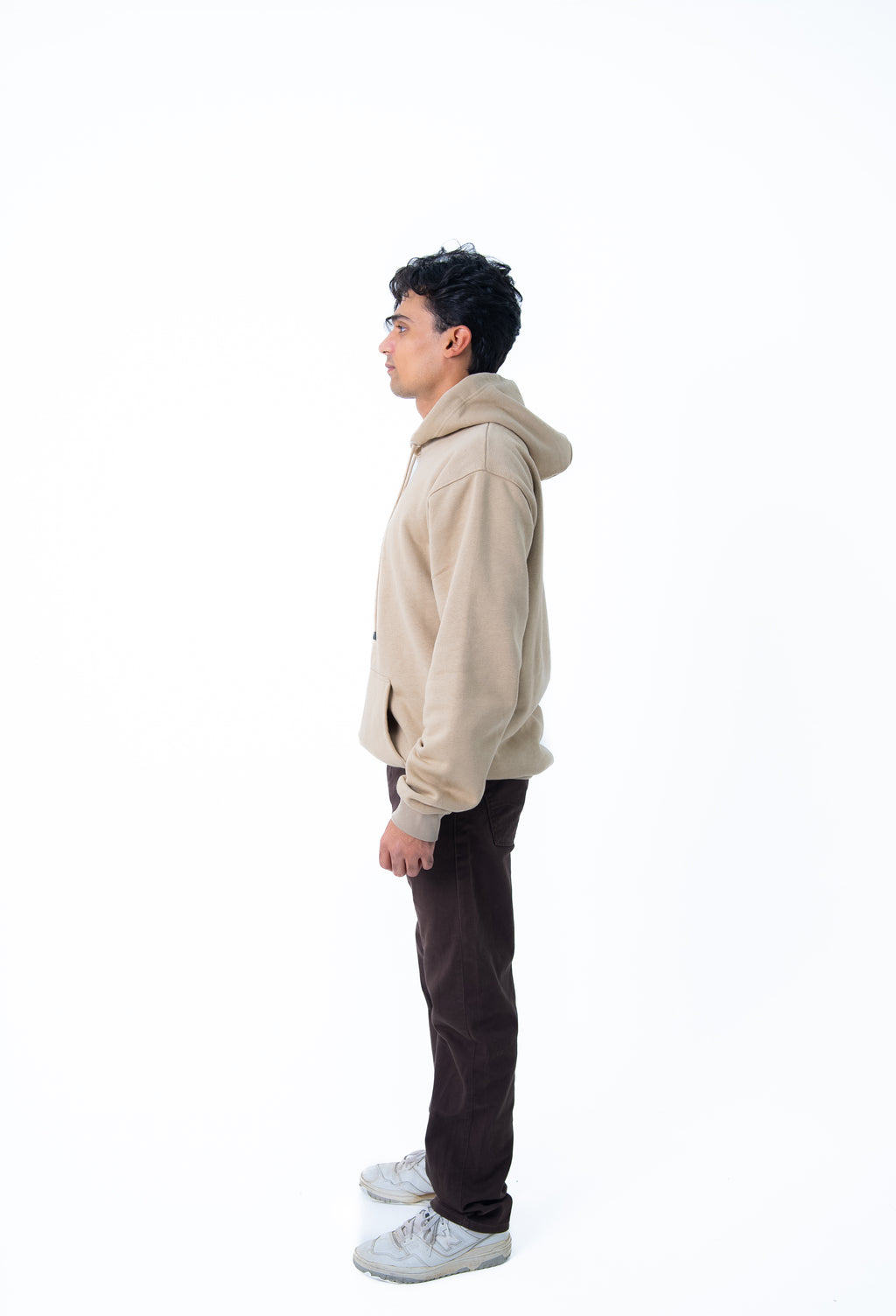 Person wearing a beige hoodie and dark pants on a white background