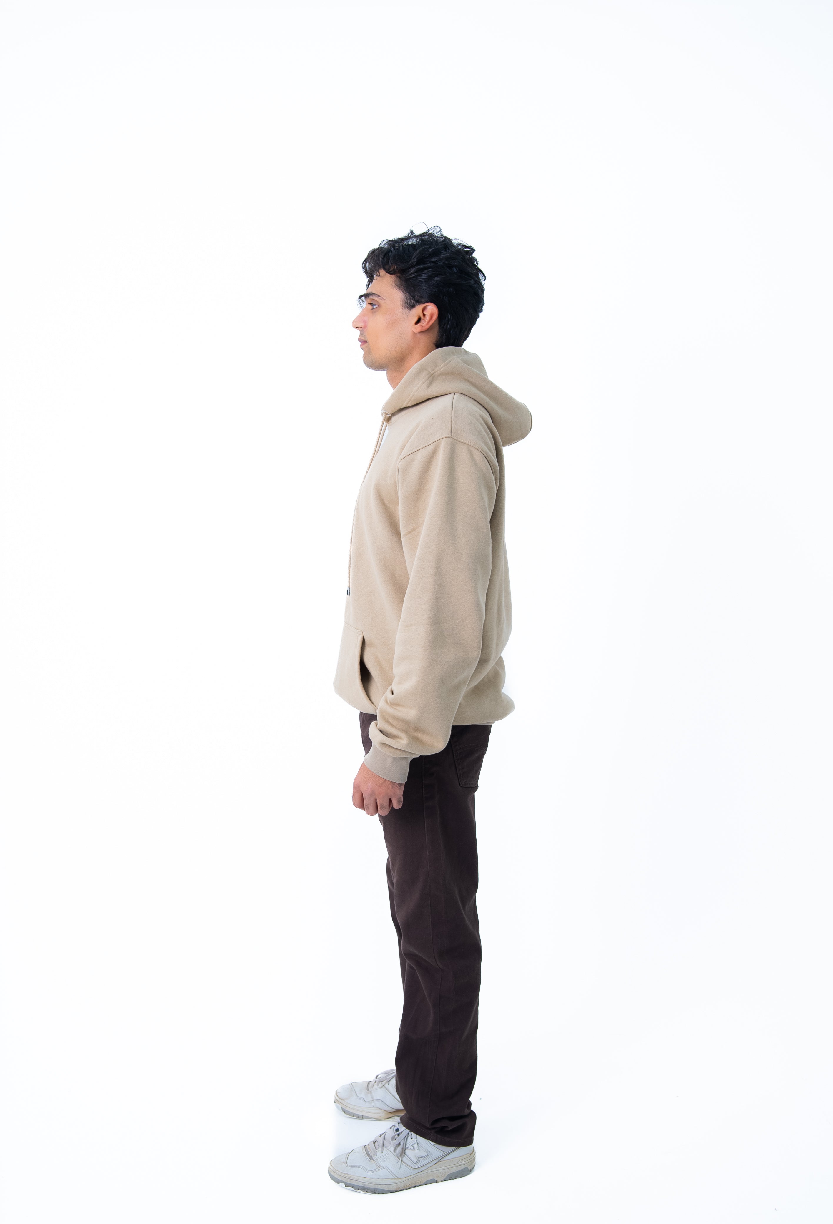 Person wearing a beige hoodie and dark pants on a white background