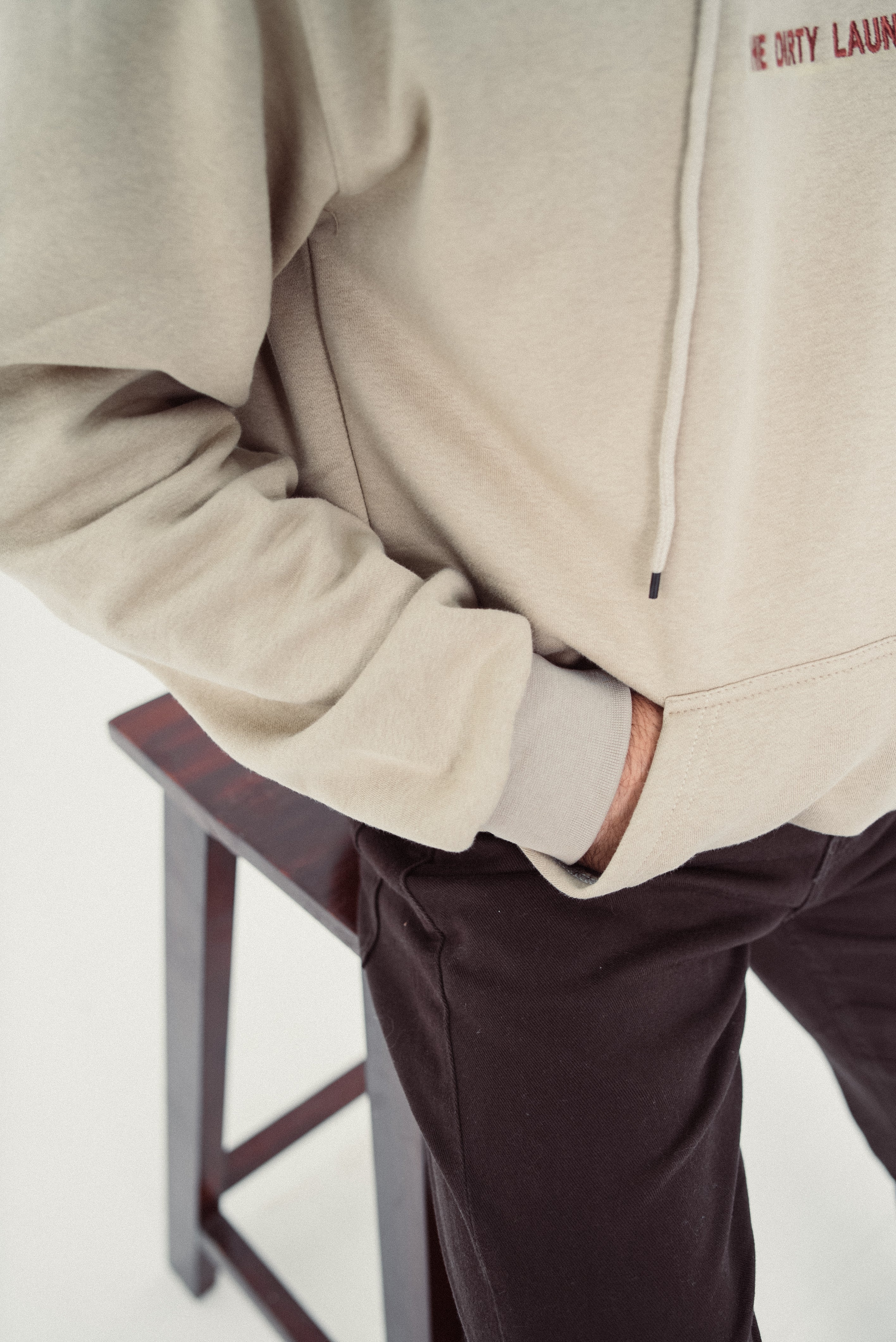 Person wearing a beige hoodie with text on it, standing next to a stool.