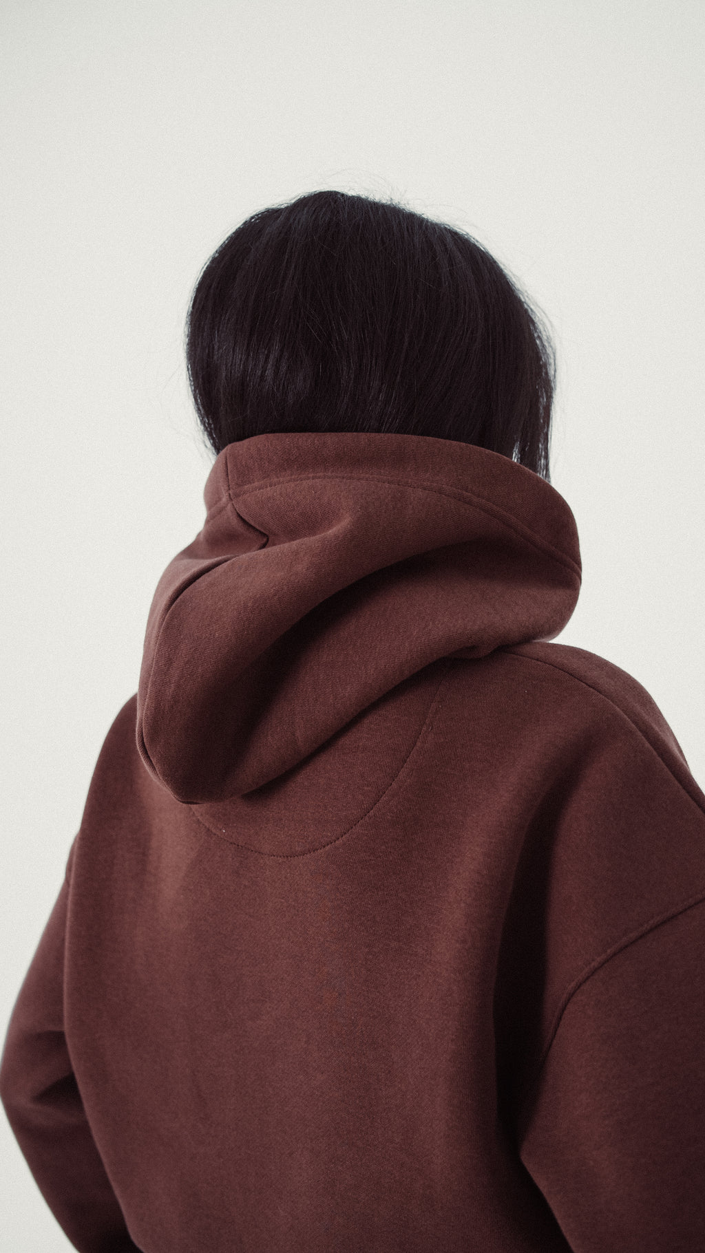 Person wearing a brown hoodie from behind on a white background