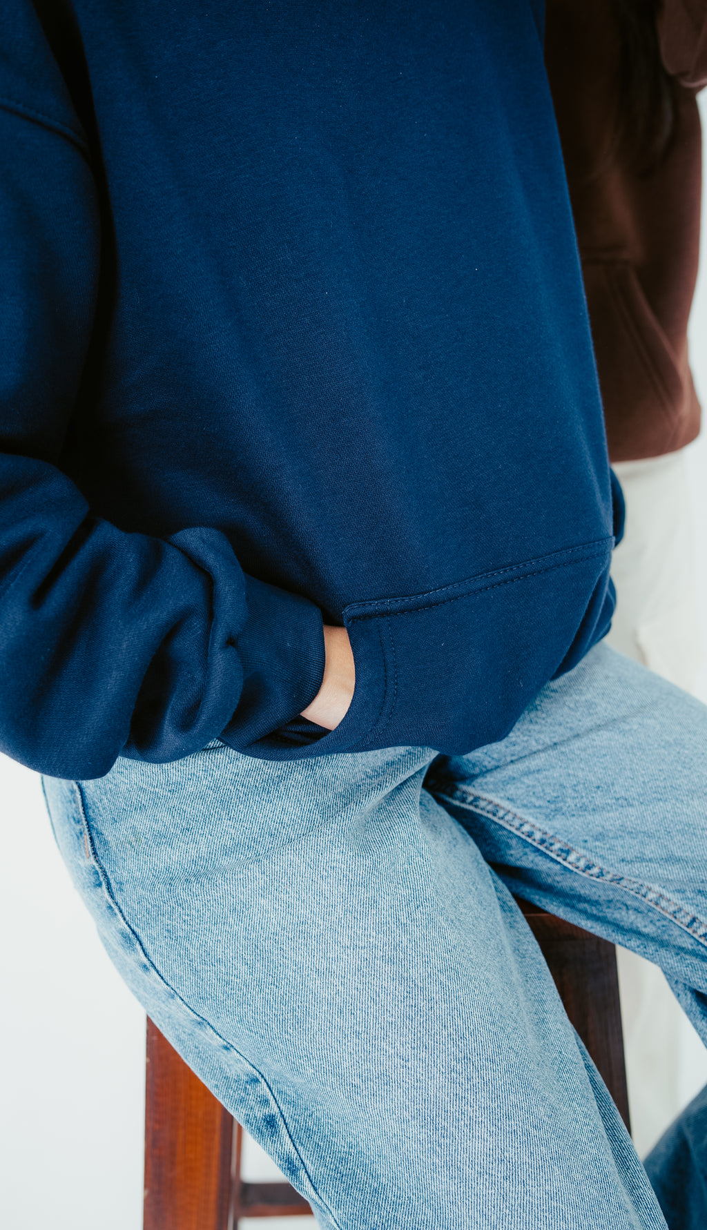 Person wearing a blue hoodie and light blue jeans sitting on a wooden stool.