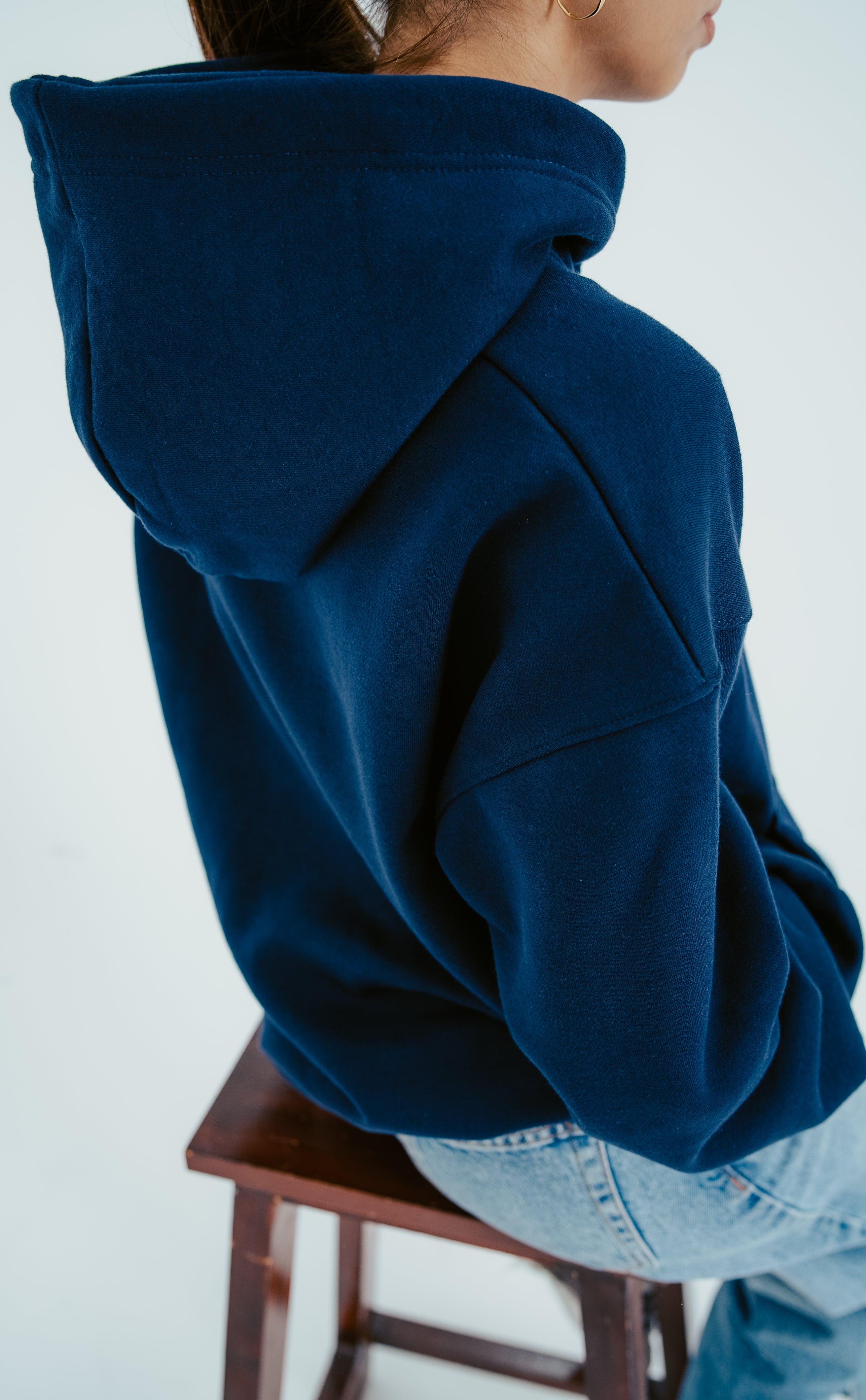 Person wearing a blue hoodie sitting on a wooden stool against a white background