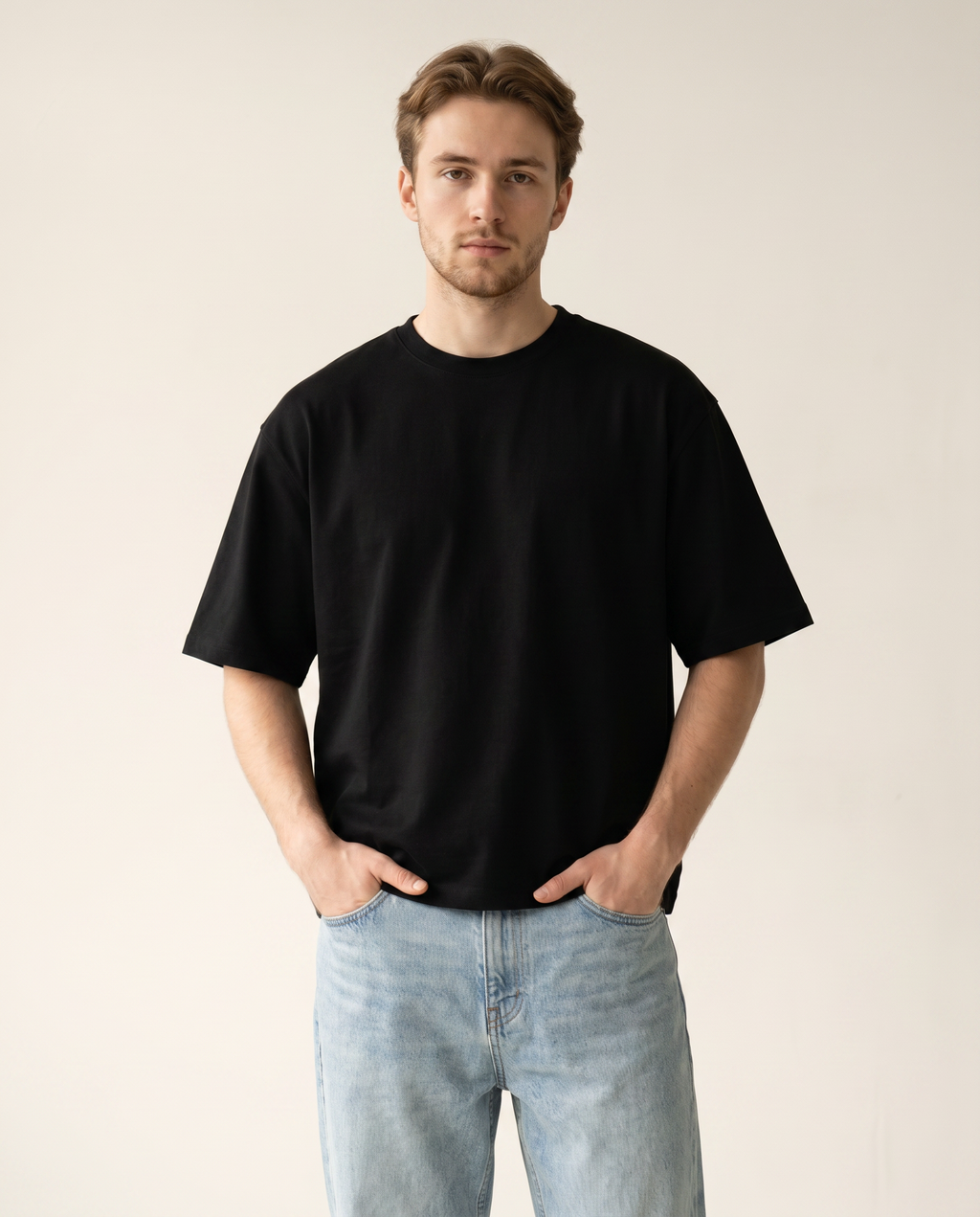 Man wearing a black t-shirt and light blue jeans against a plain background