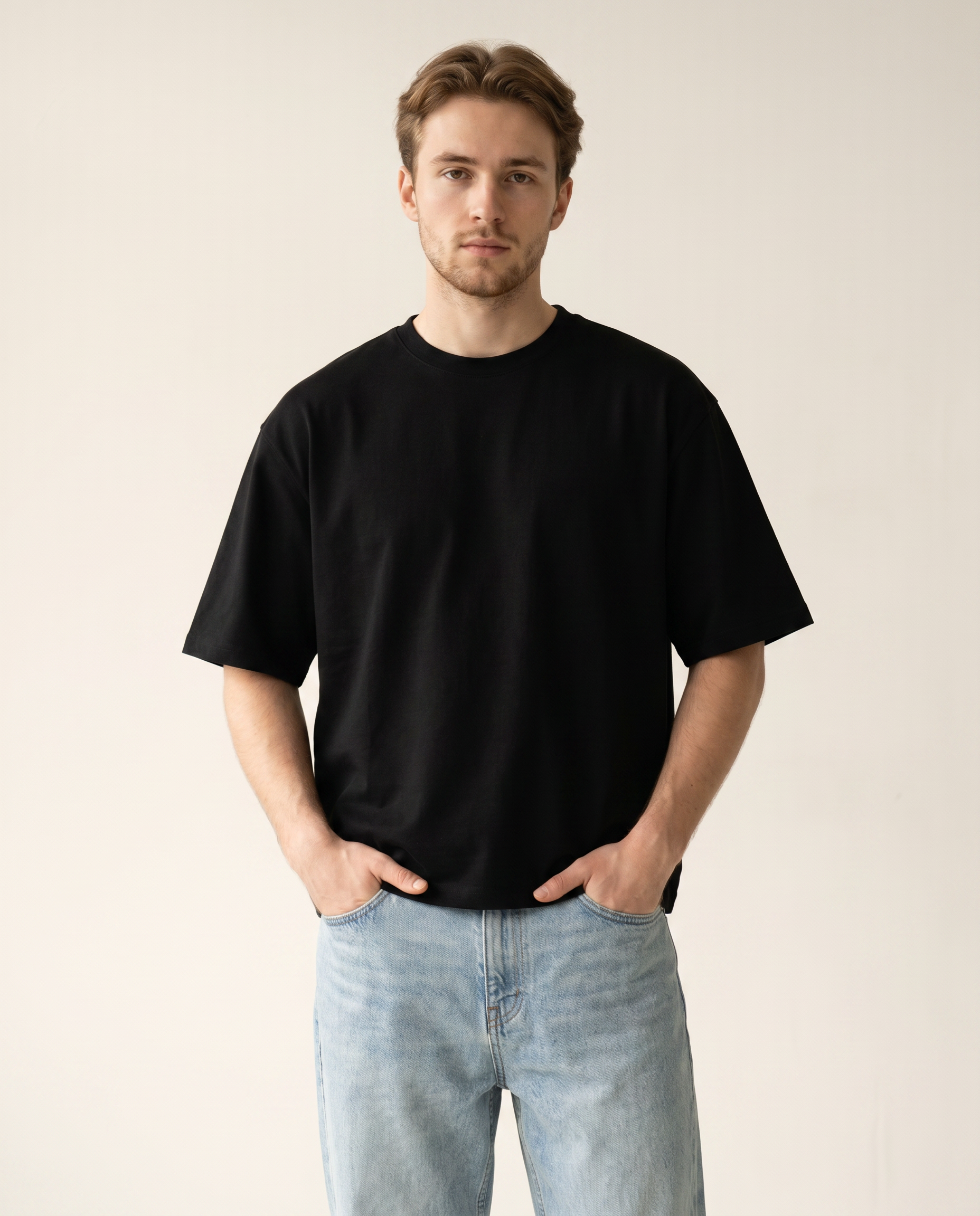 Man wearing a black t-shirt and light blue jeans against a plain background